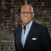 BLACK MAN IN BLUE SHIRT SMILING, WEARING BLACK BLAZER