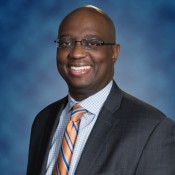 black male smiling in orange tie and grey suit jacket